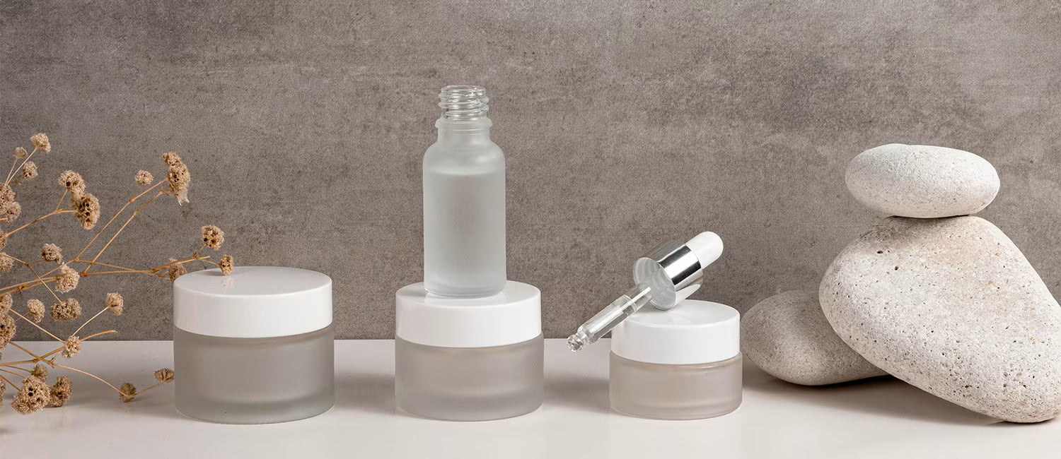 Skincare products including bottles and jars on a neutral background with stones and dried plants.